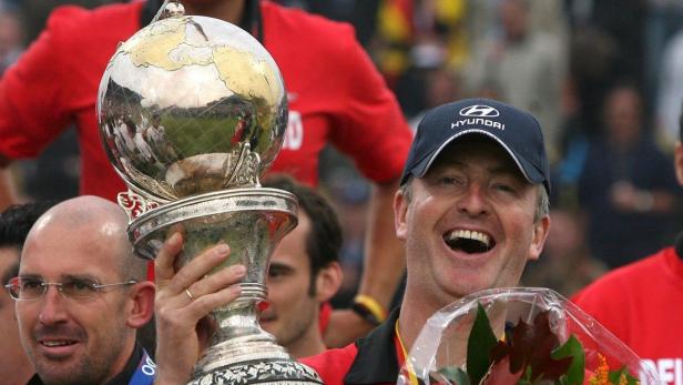 Ein Mann mit einer Hyundai-Kappe hält freudestrahlend eine Weltpokal-Trophäe in den Händen.