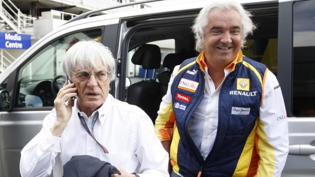 Bernie Ecclestone telefoniert neben Flavio Briatore vor einem silbernen Van.
