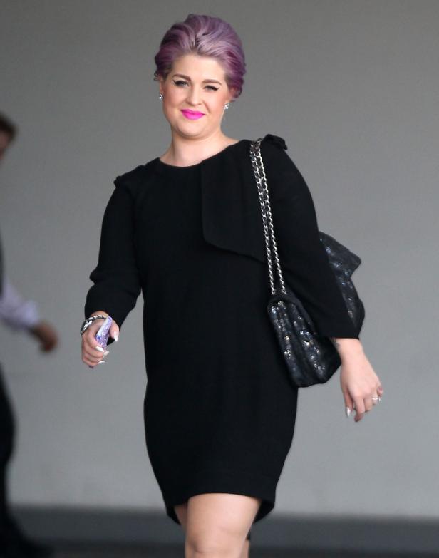 Kelly Osbourne in einem schwarzen Kleid mit lila Haaren und pinkem Lippenstift.