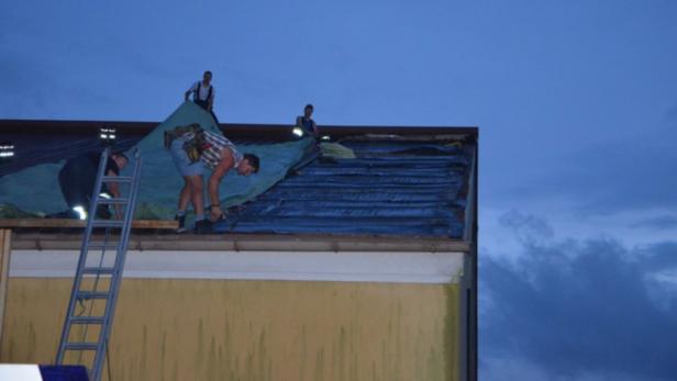 Mehrere Personen arbeiten auf einem Dach, das mit einer blauen Plane abgedeckt ist.