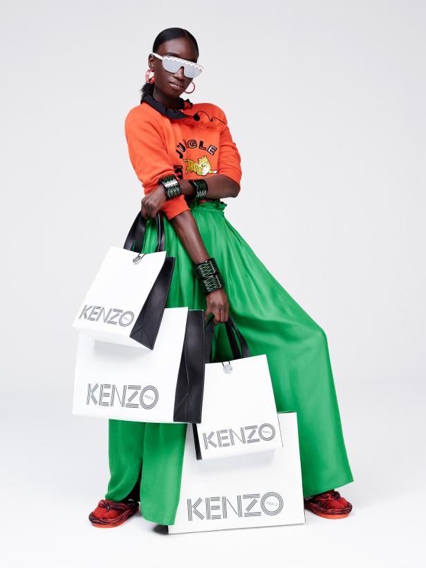 Eine Frau mit Sonnenbrille und Einkaufstüten der Marke Kenzo.