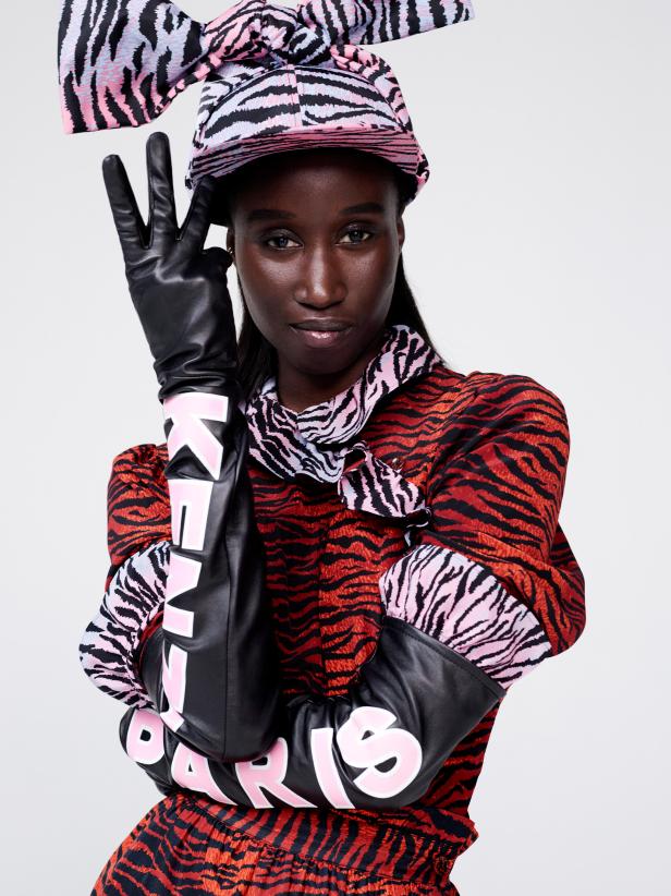 Eine Frau mit Zebra-Print-Hut und -Kleidung, sowie schwarzen Handschuhen mit der Aufschrift „KENZO PARIS“.