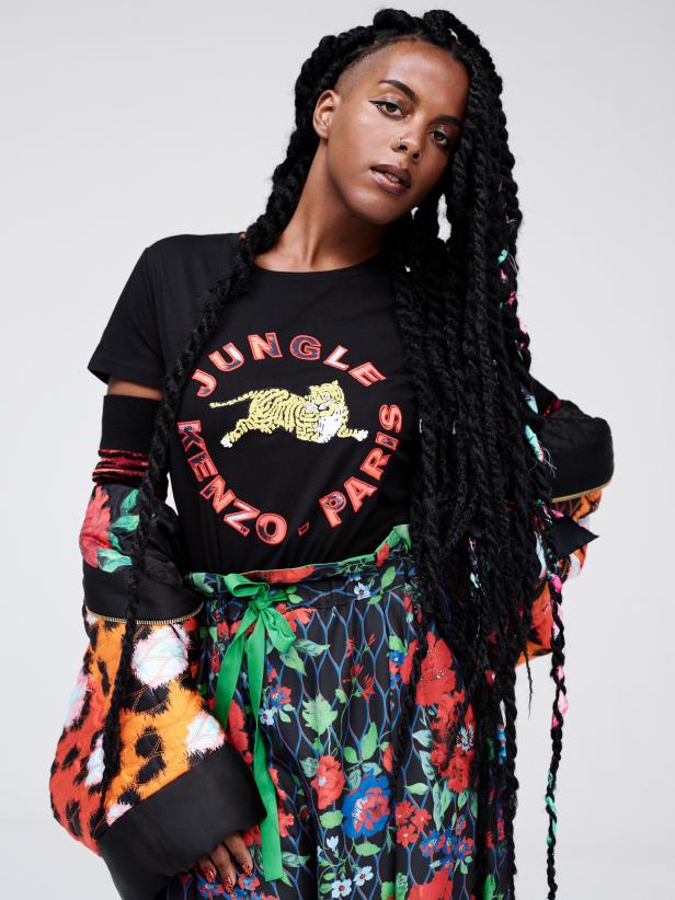 Eine Frau mit Zöpfen trägt ein T-Shirt von Kenzo Jungle und einen geblümten Rock.