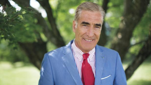 Ein lächelnder Mann in einem blauen Anzug und roter Krawatte steht im Grünen.