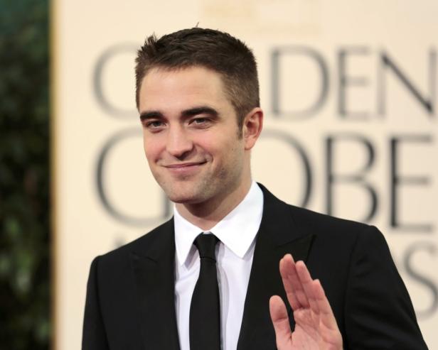 Robert Pattinson lächelt und winkt bei einer Preisverleihung.