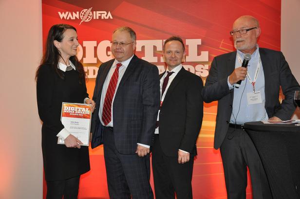 Eine Frau nimmt eine Auszeichnung bei den Digital Media Awards entgegen, während drei Männer zusehen.