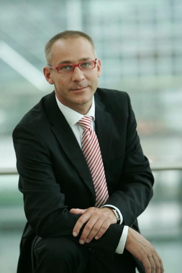 Ein Mann mit Brille und Anzug schaut in die Kamera.
