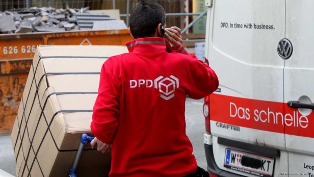 Ein DPD-Mitarbeiter transportiert ein großes Paket mit einem Rollwagen.
