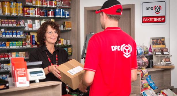 Eine Frau nimmt in einem DPD-Paketshop ein Paket von einem Boten entgegen.