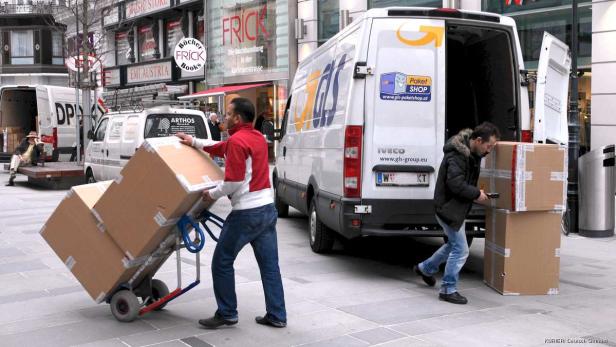 Zwei Männer entladen Pakete aus Lieferwagen in einer städtischen Umgebung.