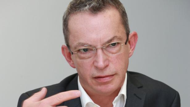 Ein Mann mit Brille und Anzug gestikuliert mit der Hand.