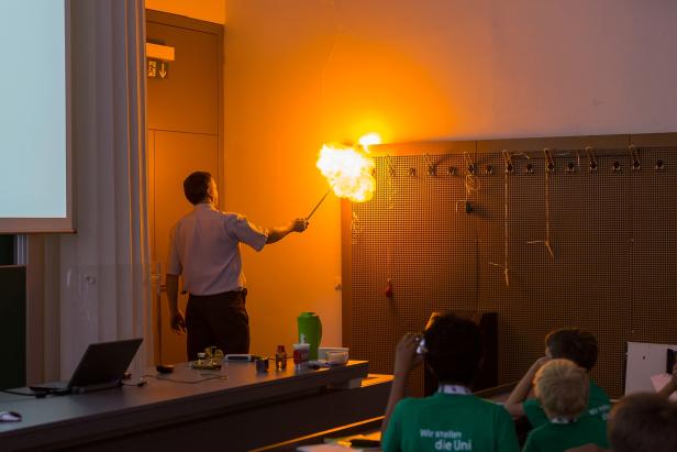 Ein Mann führt im Hörsaal ein Experiment mit einer Stichflamme vor Publikum durch.