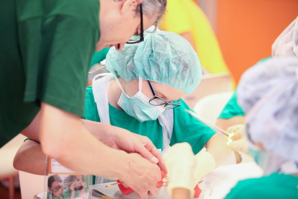 Ärzte führen eine Operation mit Mundschutz und Hauben durch.