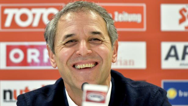 Ein lächelnder Mann vor einer Wand mit Logos.