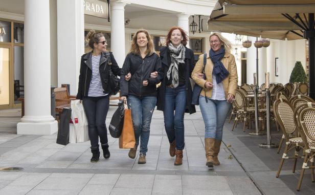 Vier Frauen gehen mit Einkaufstüten vor einem Prada-Geschäft entlang.