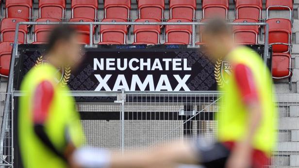Zwei Personen stehen vor einer Tribüne mit der Aufschrift „Neuchâtel Xamax“.