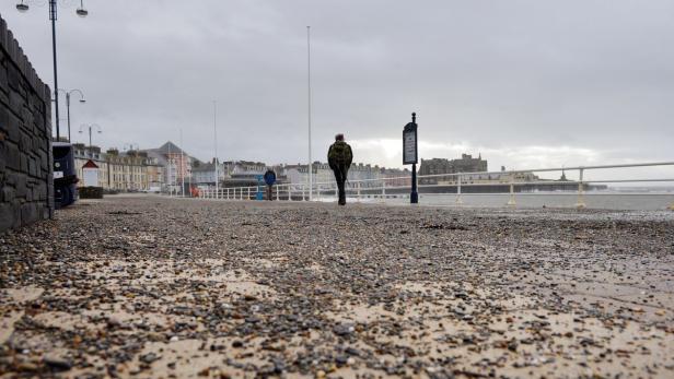 Ein Mann geht auf einer Promenade am Meer entlang.