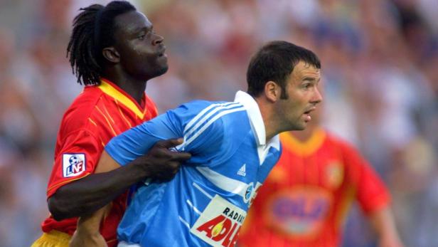 Ein Fußballspieler im roten Trikot hält einen anderen im blauen Trikot fest.