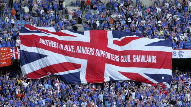 Eine große Union-Jack-Flagge mit der Aufschrift „Brothers in Blue, Rangers Supporters Club, Shawlands“ wird von Fußballfans gehalten.