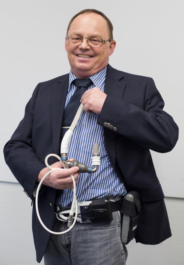 Ein lächelnder Mann im Anzug präsentiert ein medizinisches Gerät, das an seinem Gürtel befestigt ist.