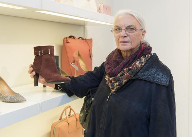 Eine ältere Frau betrachtet einen braunen Stiefeletten in einem Schuhgeschäft.