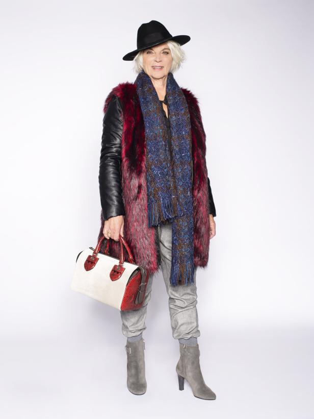 Eine Frau mit Hut, Schal und Pelzmantel posiert mit einer Handtasche.