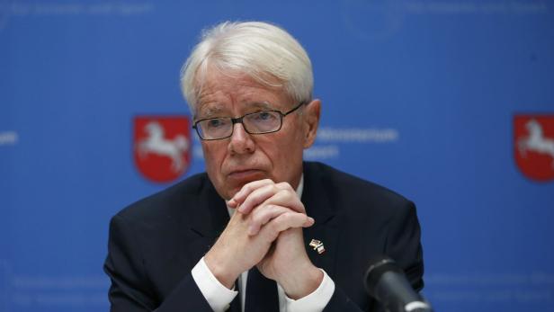 Ein Mann mit Brille und weißem Haar sitzt vor einem blauen Hintergrund.