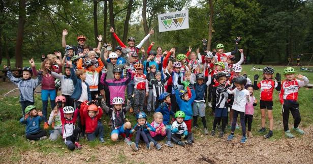 Eine Gruppe Kinder und Erwachsene posiert mit Helmen vor einem „Wienerwaldtrails“-Schild.