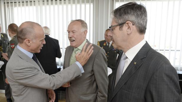 Drei Männer in Anzügen unterhalten sich in einem Raum.