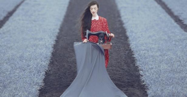 Eine Frau mit rotem Kleid und Nähmaschine steht auf einem Feld.