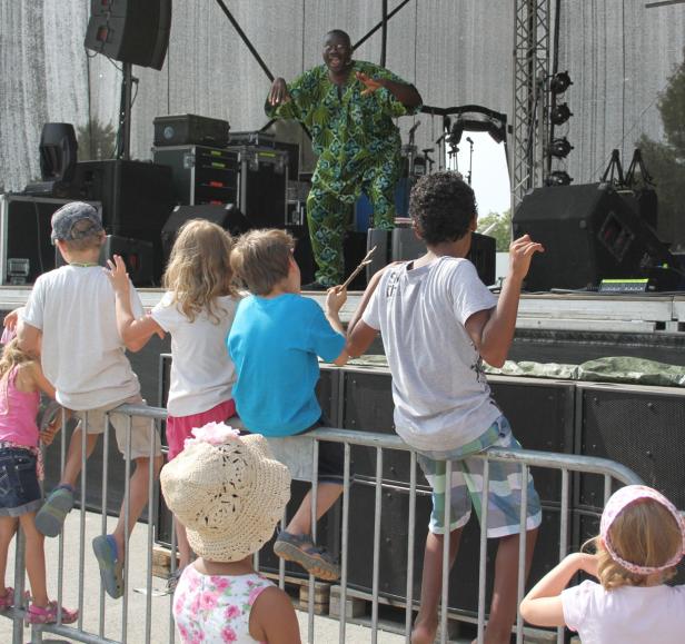 Ein Mann in einem grünen Anzug tanzt auf einer Bühne vor einer Gruppe von Kindern.
