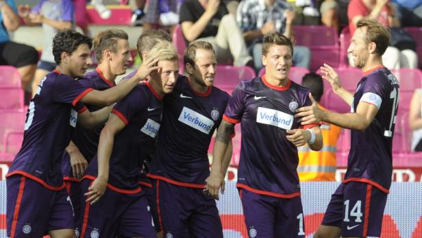 Eine Gruppe Fußballspieler in lila Trikots feiert gemeinsam auf dem Spielfeld.