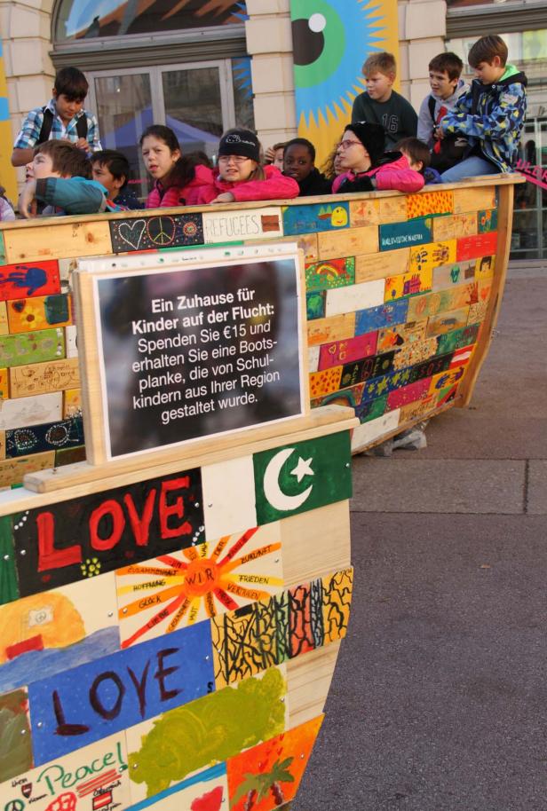 Kinder stehen und sitzen in einem bemalten Holzboot mit der Aufschrift „Love“ und „Peace“.