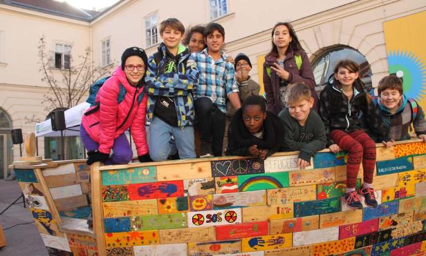 Eine Gruppe von Kindern steht und sitzt auf einem bemalten Holzboot.