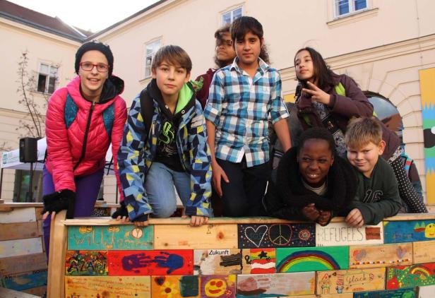 Eine Gruppe von Kindern steht hinter einer bemalten Barrikade mit der Aufschrift „Willkommen“.