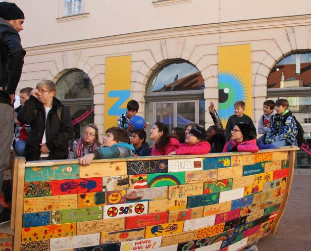 Eine Gruppe Kinder sitzt in einem bemalten Holzboot vor dem Deutschen Museum.
