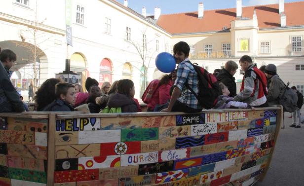 Eine Gruppe von Kindern sitzt auf einem bemalten Holzboot vor einem Gebäude.