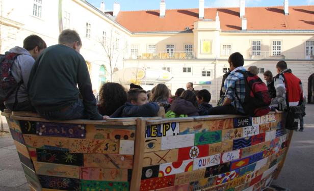 Eine Gruppe von Kindern sitzt in einem bemalten Holzboot auf einem Platz.
