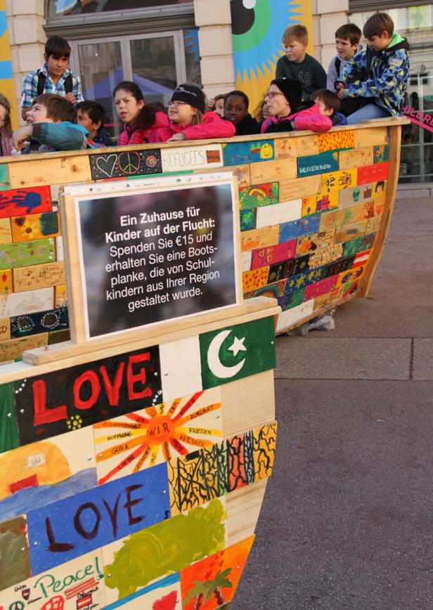 Kinder stehen in einem bemalten Holzboot mit der Aufschrift „Love“ und Friedensbotschaften.
