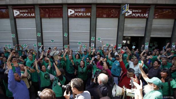 Eine Menschenmenge in grünen T-Shirts demonstriert vor einer Banco Popular Filiale.