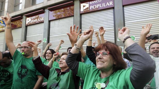 Menschen demonstrieren vor einer Banco Popular Filiale mit erhobenen Fäusten.
