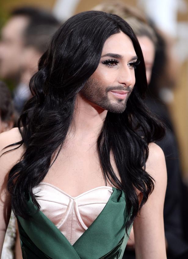 Conchita Wurst mit langem, dunklem Haar und Bart in einem grünen Kleid.