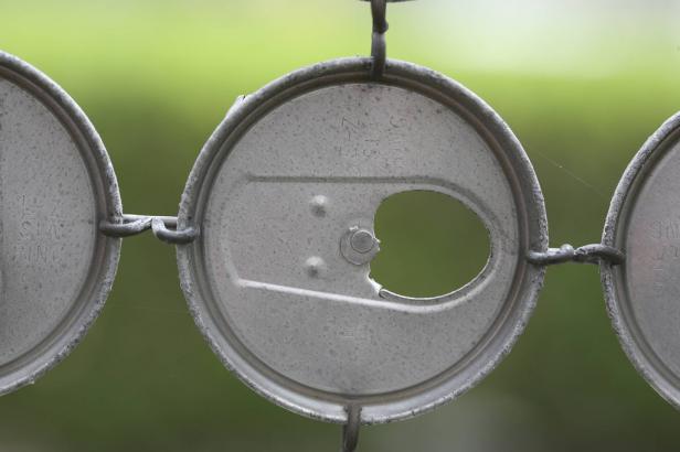 Mehrere miteinander verbundene, recycelte Getränkedeckel vor einem grünen Hintergrund.