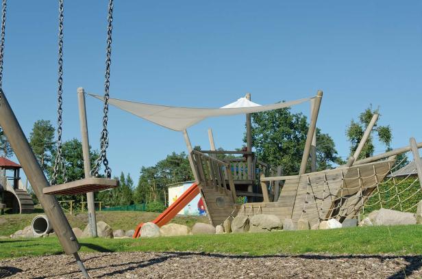 Ein Spielplatz mit einer Schaukel und einem hölzernen Schiff mit Rutsche.