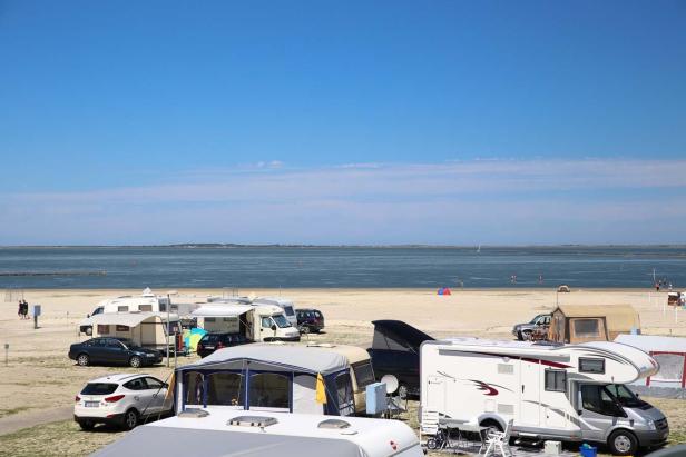 Ein Campingplatz mit Wohnwagen und Zelten an einem Strand mit blauem Himmel.