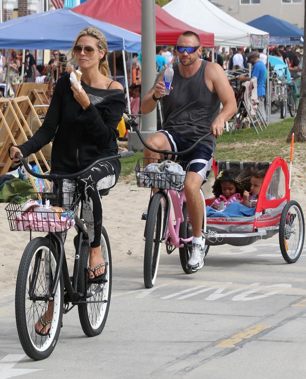 Heidi Klum fährt mit ihrem Mann und ihren Kindern in einem Fahrradanhänger am Strand entlang.