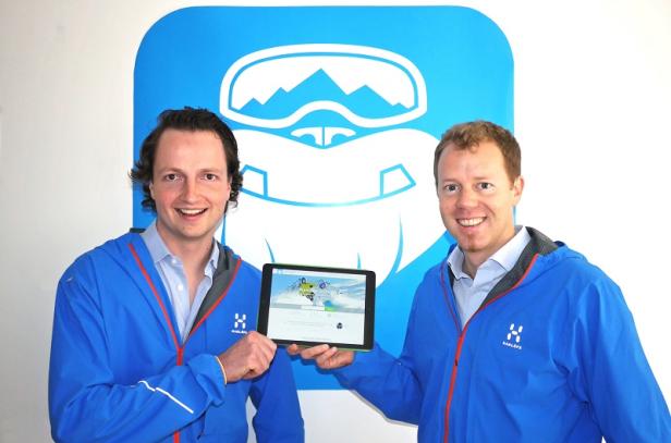 Zwei Männer in blauen Jacken präsentieren eine Tablet-App vor einem Yeti-Logo.