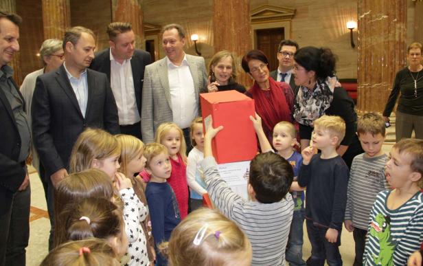 Eine Gruppe von Kindern und Erwachsenen steht um eine rote Kiste herum.