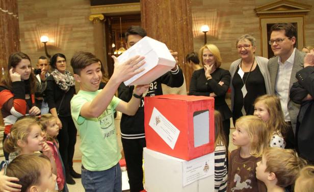Ein junger Mann öffnet eine Box vor einer Gruppe von Kindern und Erwachsenen.