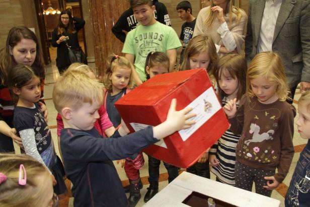 Eine Gruppe Kinder betrachtet eine große, rote Spendenbox.